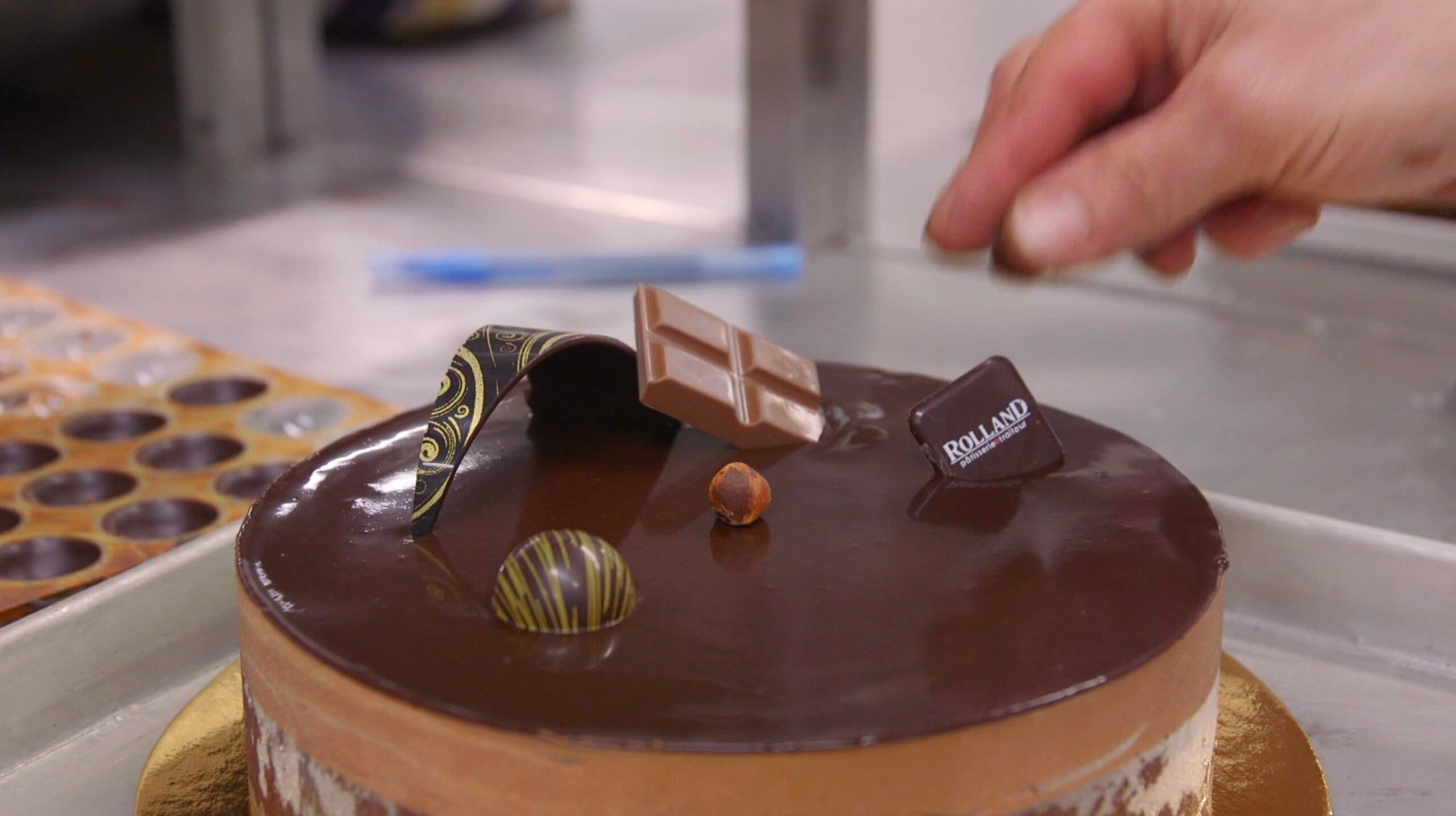 Pâtissier posant un décor sur un gâteau au chocolat dans l'atelier Rolland